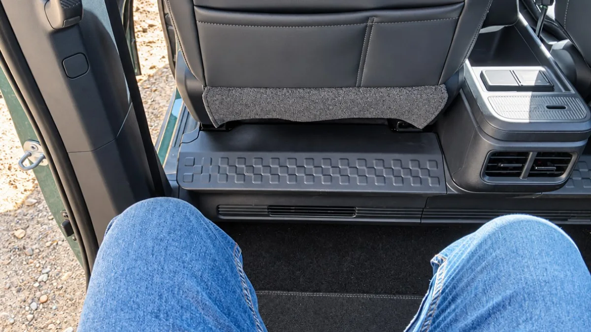 Vista en primera persona del espacio para las piernas en los asientos traseros de un automóvil, mostrando a una persona con vaqueros azules sentada frente al respaldo del asiento delantero y la consola central con salidas de aire.