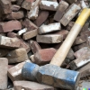 A photograph of a sledgehammer leaning against a pile of bricks and rubble.