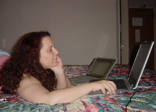 In this photo Molly is lying on her stomach on a hotel bed with two laptops open. She’s working on our slide deck.