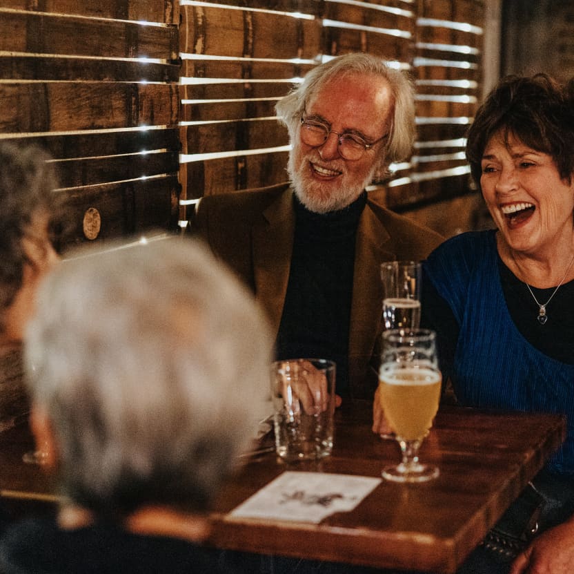 Ruby and Jack sitting across from Peggy and John at a cosy side table, laughing over drinks and dinner