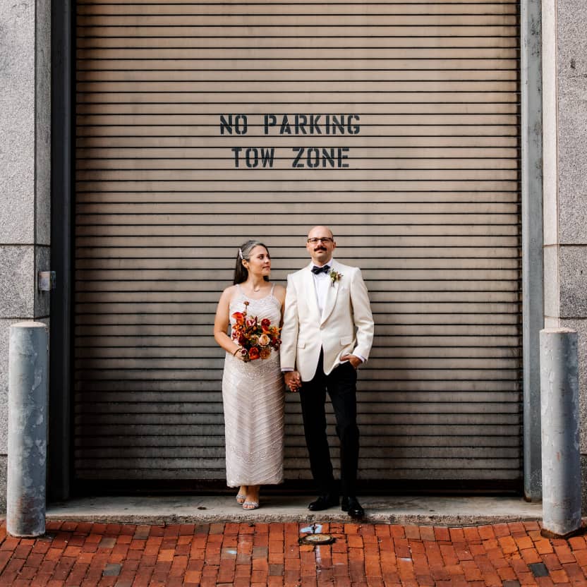 Andrew & Meredith standing side by side in front of a giant industrial looking loading door that says No Parking Tow Zone