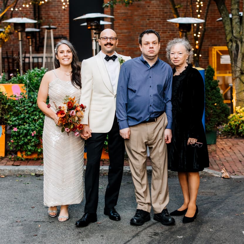 Meredith & Andrew and his mom and brother, posing in front of a patio with string lights