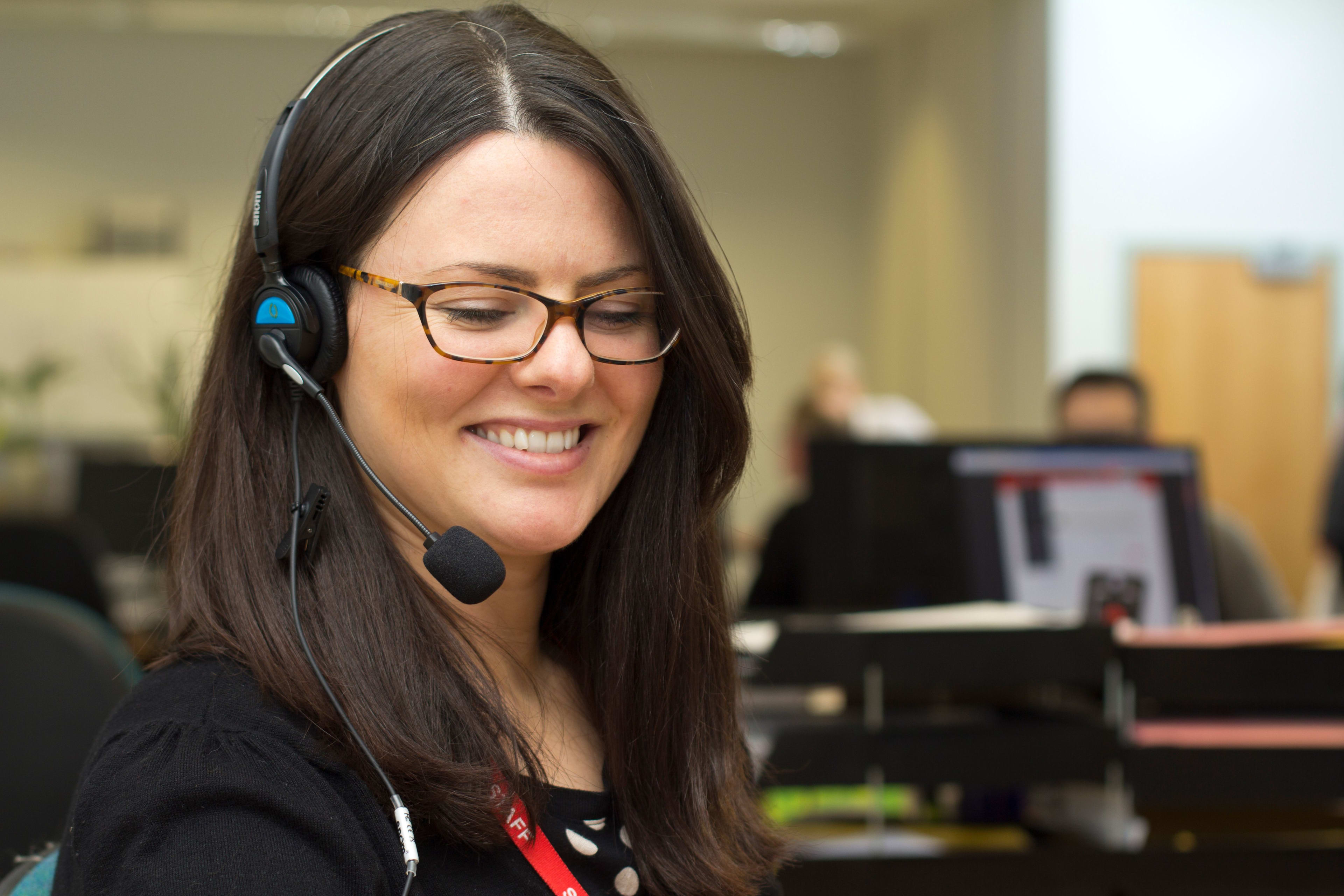 A woman smiling whilst taking a call on a headset