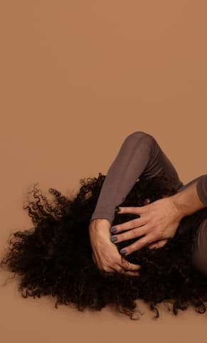 Woman with dark curly hair covering her face, lying on the ground.