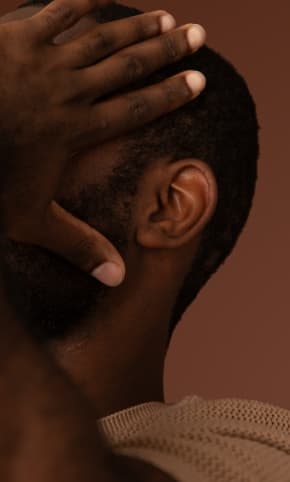 A man holding his head in his hands, such that his face is covered, facing off camera