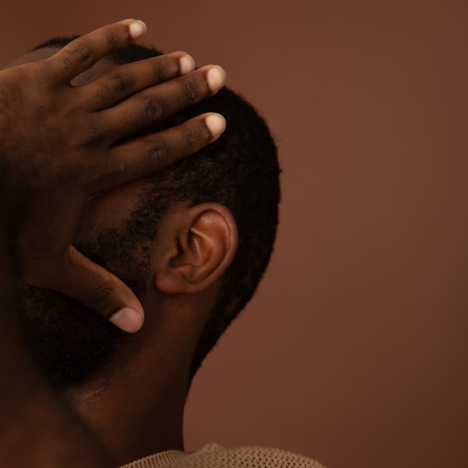 A man holding his head in his hands, such that his face is covered, facing off camera