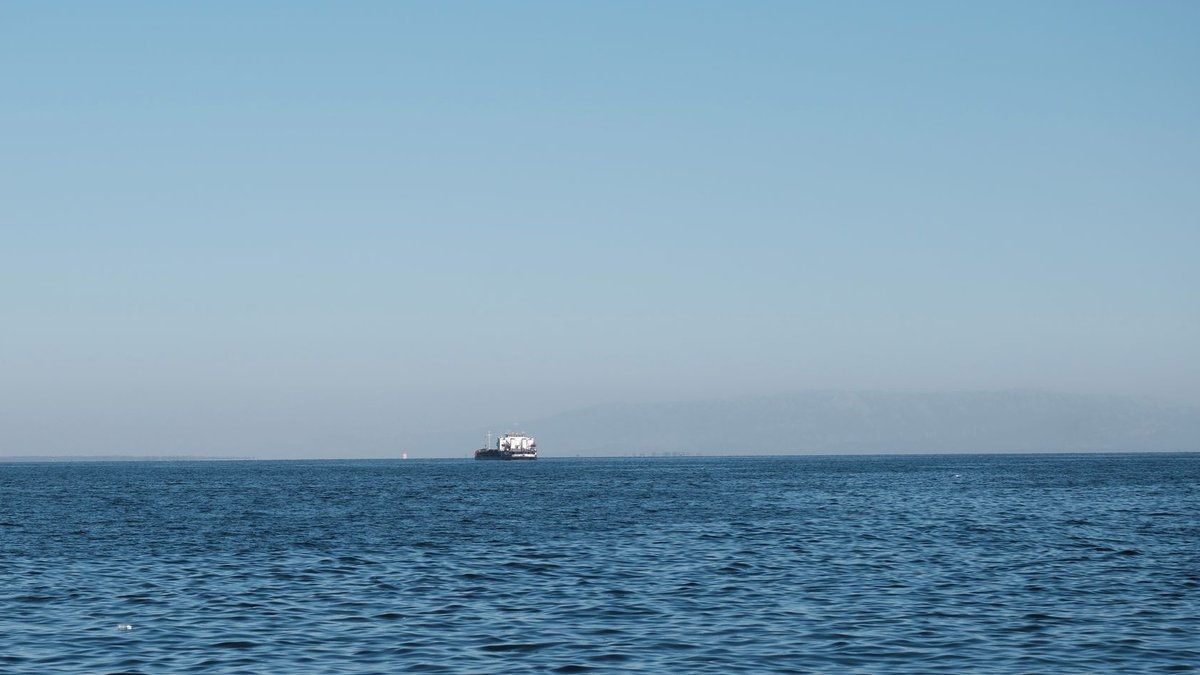 U.S. Iran Revive Talks to Resolve Hormuz Standoff A serene scene of a ferry traversing the calm waters of İzmir Gulf under a clear blue sky.
