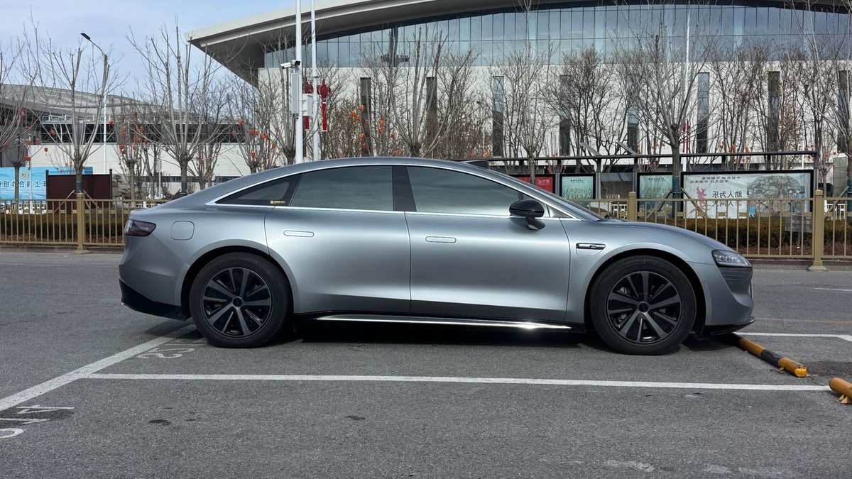 XPeng Launches Six-Variant Lineup in Philippines Side view of a sleek silver electric sedan parked in a city lot by a modern building.