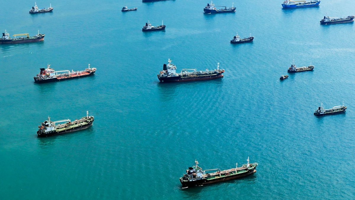 Insurers warn of rising risks Numerous cargo ships anchored on the blue ocean, captured from above.