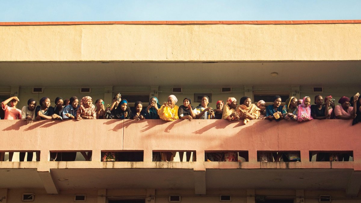 A large group of women in colorful attire enjoying a sunny day outdoors on a building patio.