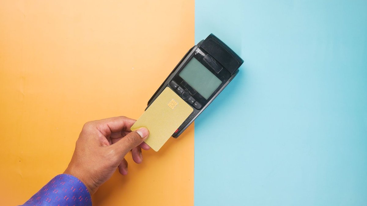 A hand tapping a credit card on a payment terminal for a contactless transaction.
