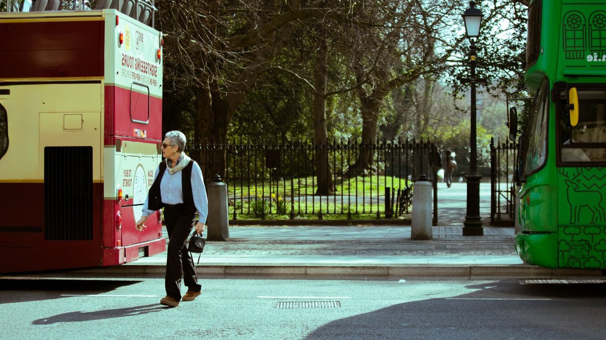 Irish Tourism's 40 Under 40 Winner to Be Announced Thursday A man walks between two tour buses on a sunny day in Dublin, Ireland, highlighting urban travel vibes.