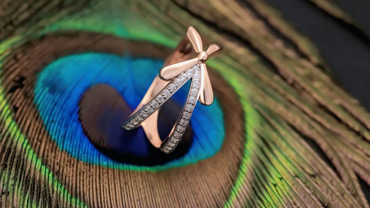 Rose gold ring with diamonds elegantly displayed on a vivid peacock feather for a luxurious touch.