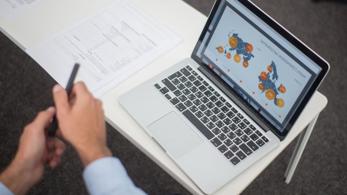 Remote Work in Southeast Asia Poses Legal Challenges for Employers Professional analyzing data infographics on a laptop at an office desk, featuring documents and a pen.