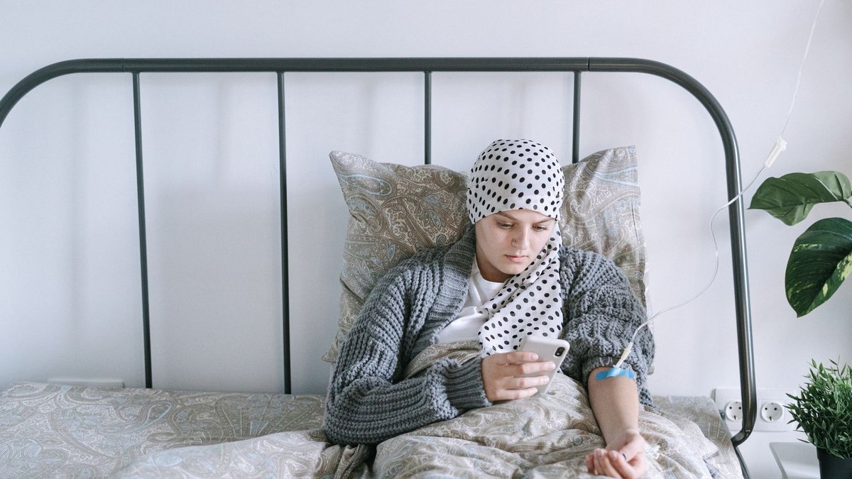 Breakthrough pancreatic cancer drug doubles survival in late-stage patients A woman undergoing chemotherapy checks her smartphone in a hospital bed, symbolizing hope and recovery.