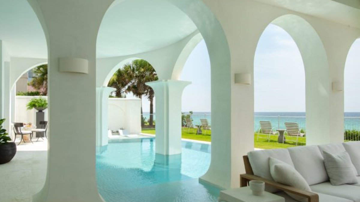 Florida Beach House Features Greek Inspired Poolscape Aegean blue pool water flows around arched white columns overlooking the Gulf.