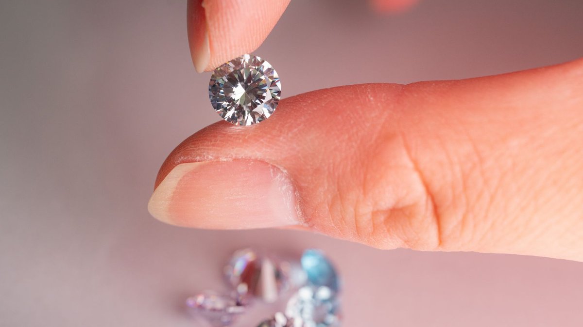 A detailed macro shot showing a hand holding a sparkling diamond with several gems in the background.
