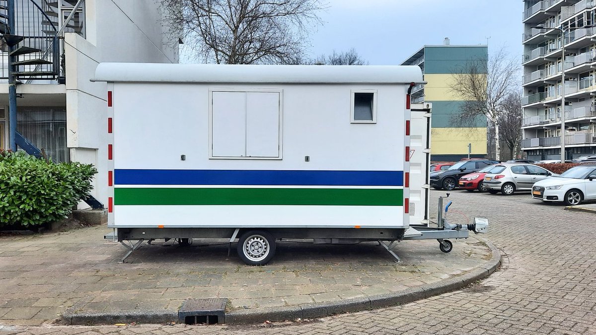 A white mobile trailer parked in an apartment complex parking lot.
