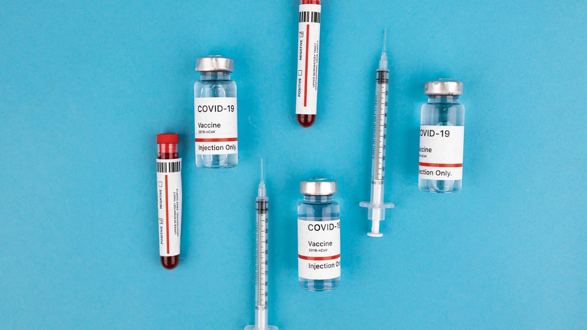 Cancer vaccine uses COVID immune memory Top view of COVID-19 vaccine vials, syringes, and test tubes on a blue background, representing immunization and protection.