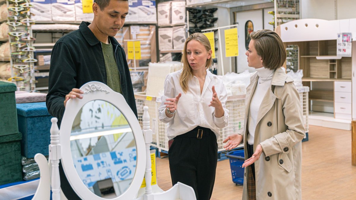 Three adults discussing a vanity set in a furniture store, engaging in shopping decisions.