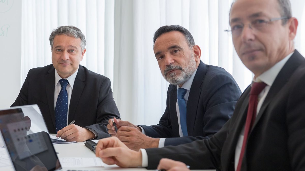 Senior executives in suits conducting a meeting in an office setting.