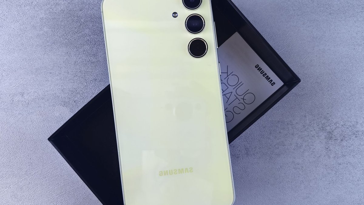 Yellow Samsung smartphone displayed on a gray surface with its box and quick start guide.