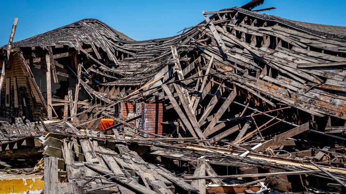 USAA issues new catastrophe bond A dramatic view of a destroyed wooden building after a catastrophe, showing debris and structural failure.