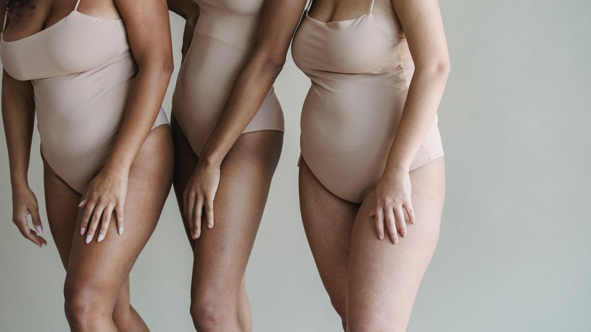 Three diverse women posing in nude bodysuits, celebrating body positivity and diversity.