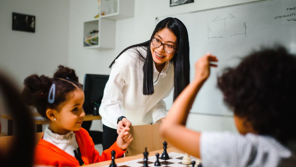 New Approach for Principals to Coach Teachers Engaging classroom scene with teacher guiding children in a chess game, fostering learning and fun.