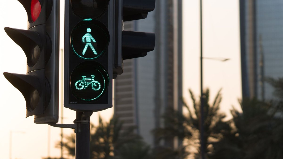 Abu Dhabi Launches 13km Road Upgrade in Mussafah Traffic light showing pedestrian and bicycle signals with Abu Dhabi skyline backdrop.