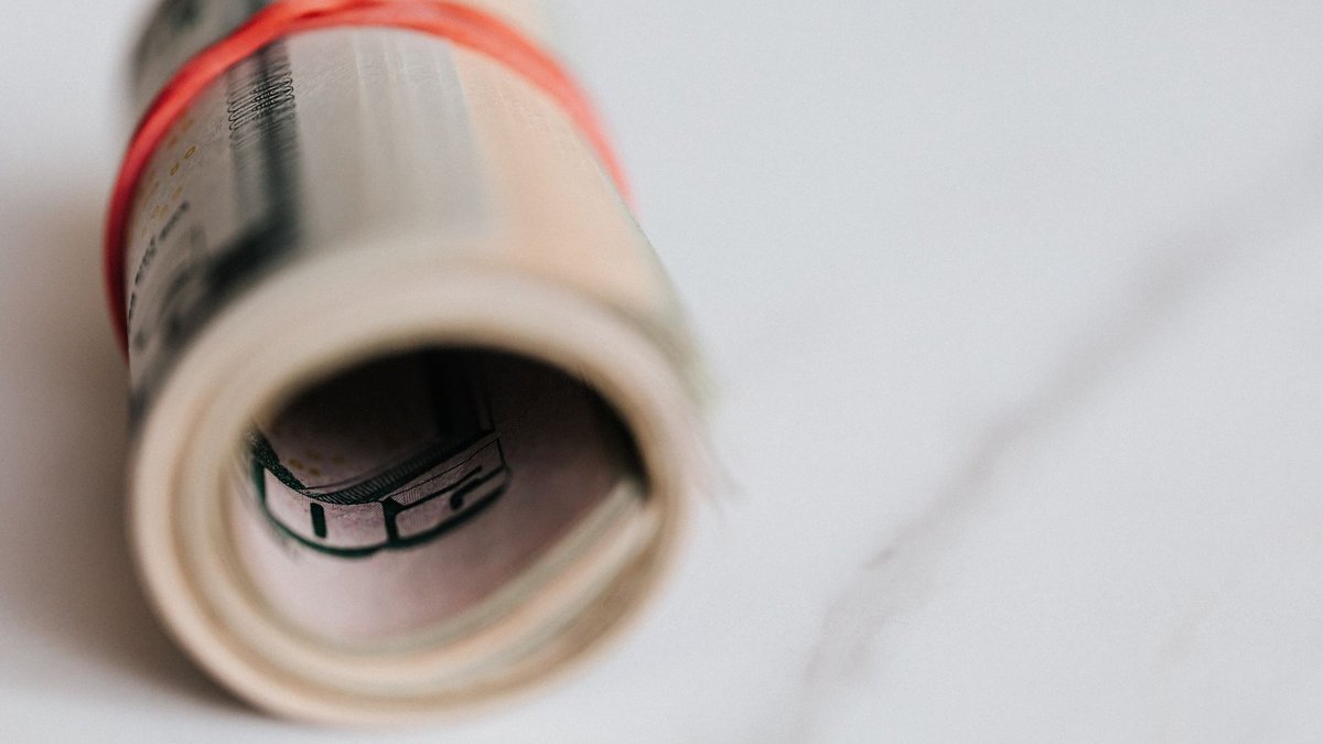 Pack of fifty dollar bills twisted into roll and tightened with red rubber band on white background.