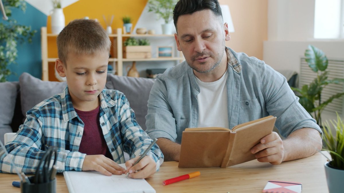 Gentle Parenting Requires Clear Boundaries and Structure Father helping son with homework in a cozy living room setting, promoting education and bonding.