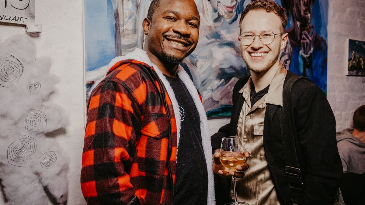 Two friends enjoying a lively art gallery event, smiling and toasting with wine.