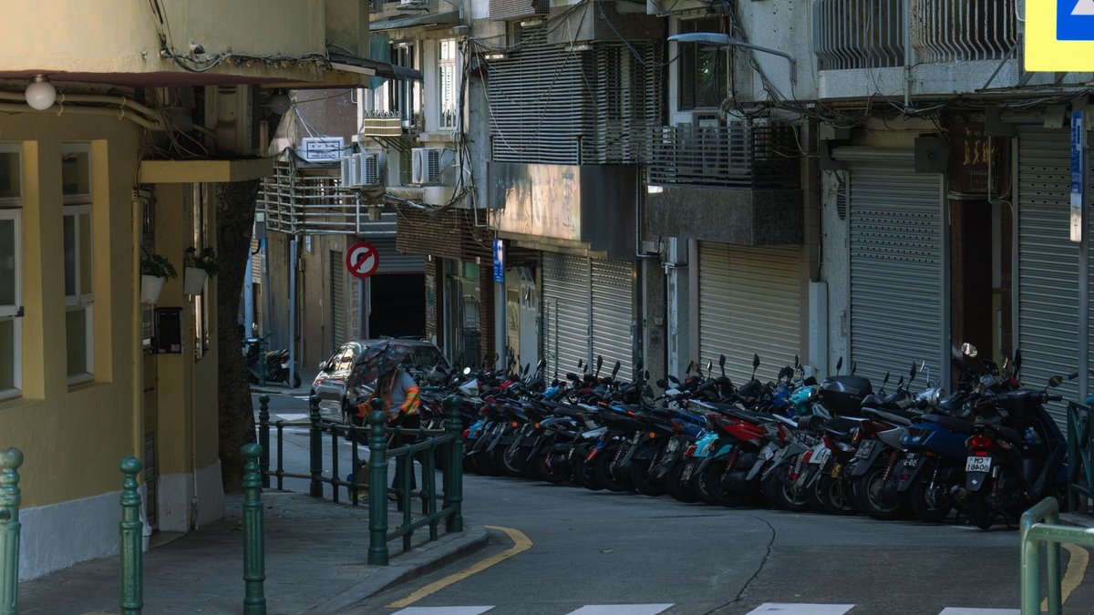 Street scene in Macau showing parked motorcycles and residential buildings in a narrow alley.