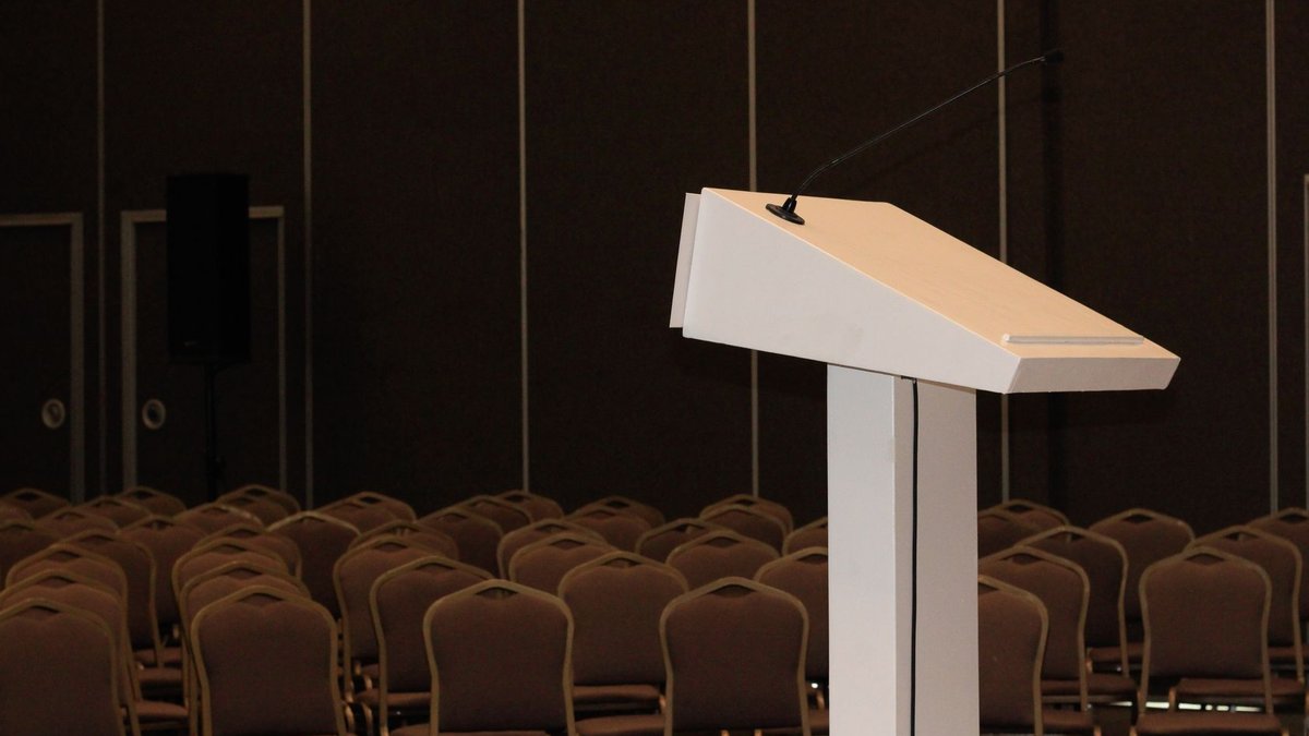 An empty conference room setup with podium and rows of chairs, ready for an event.