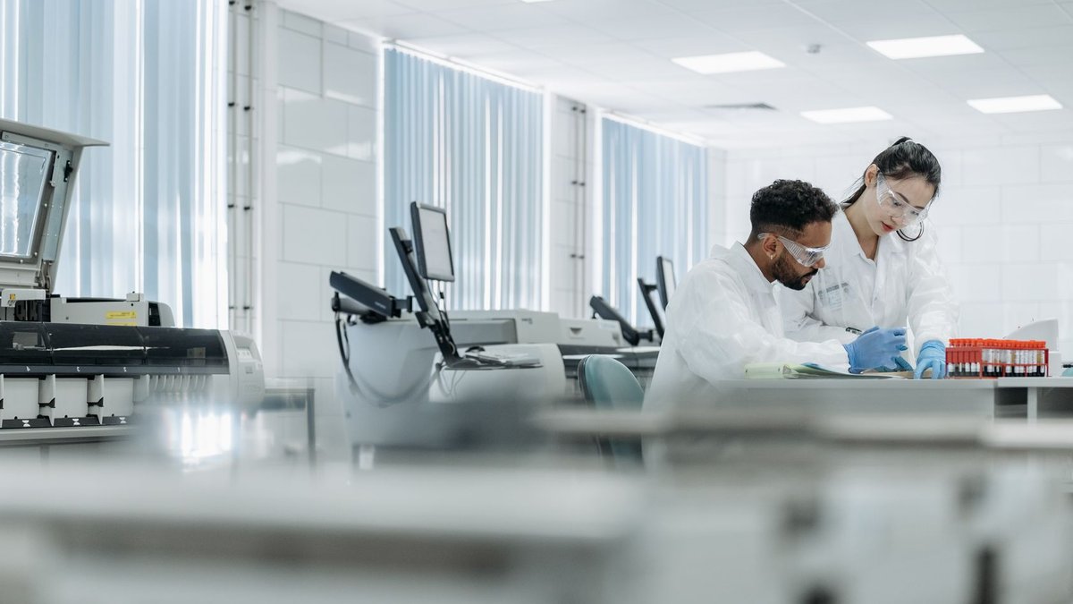 Two scientists working in a high-tech laboratory setting, wearing protective eyewear and gloves.