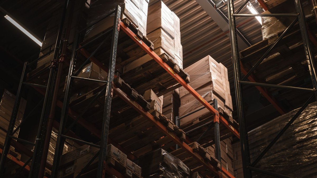 Amazon cuts prices on power tool batteries Interior view of a warehouse with stacked cardboard boxes on high shelves, showcasing storage and logistics.