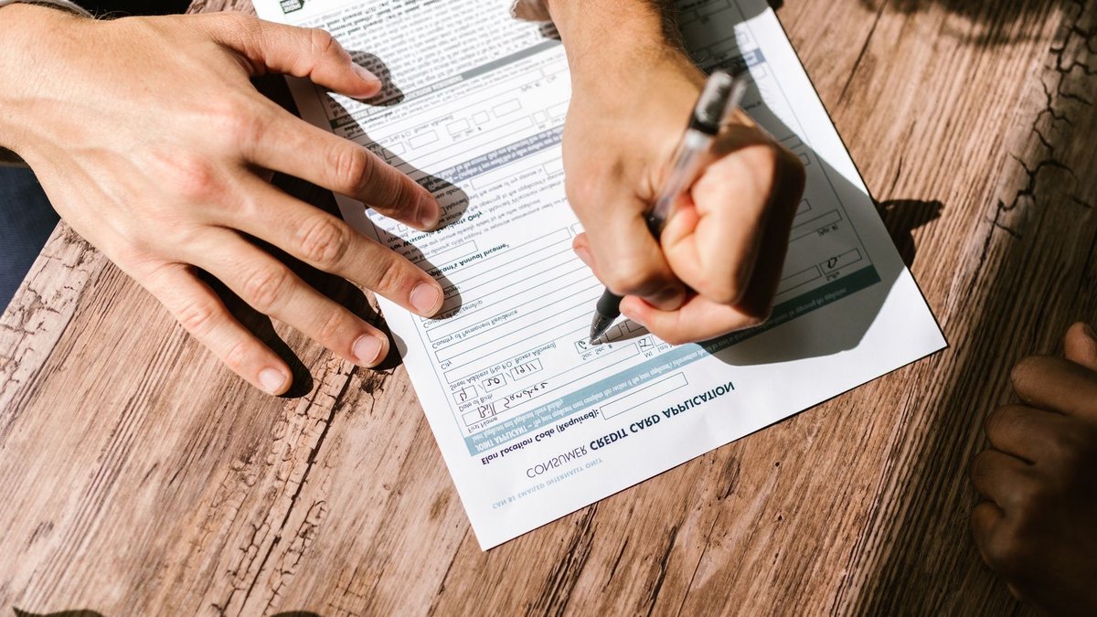 Govt Sets 30-Day Cap on Capital Repatriation Delays Hands writing on a consumer loan credit application form on a wooden table.