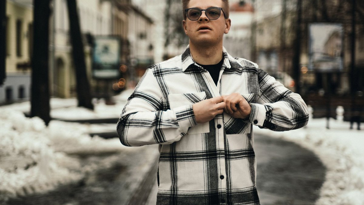 R29 unveils fall winter fashion lookbook Man in checkered shirt standing on snowy city street, conveying a modern urban winter style.