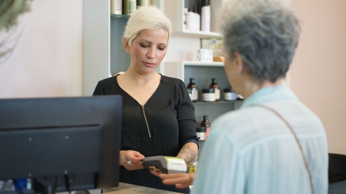 Two women at a hair salon checkout, one making a payment using a card reader.