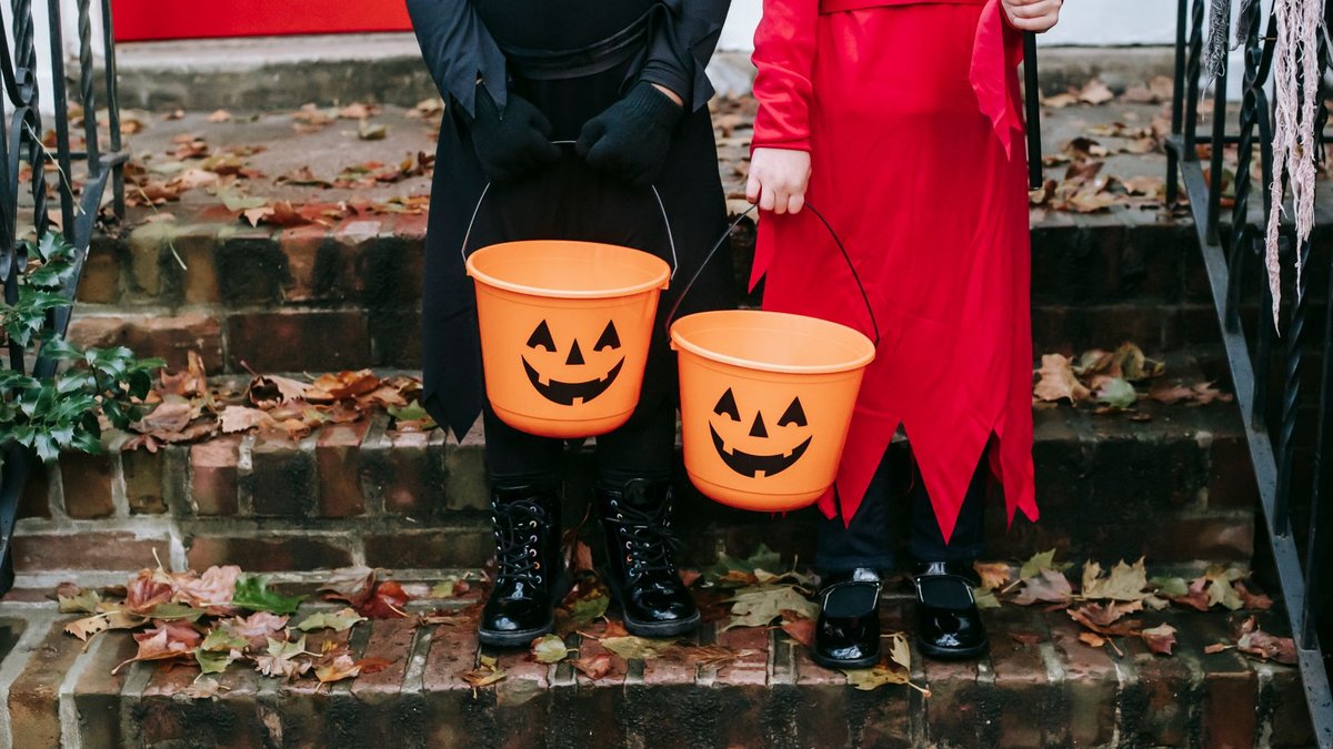 Two children in costumes holding pumpkin buckets, ready for Halloween trick-or-treating.
