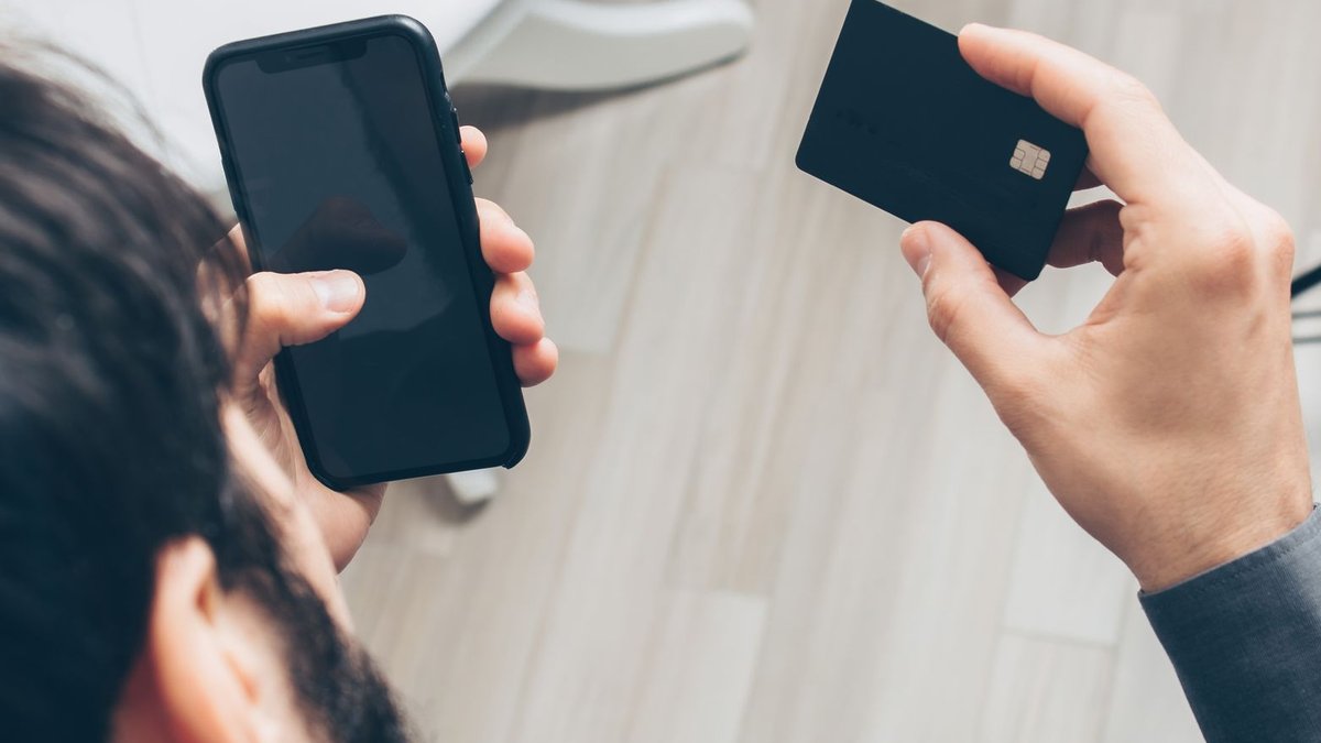 UK Launches New Scheme to Boost Commercial Open Banking Close-up of man holding a smartphone and credit card, making an online payment indoors.
