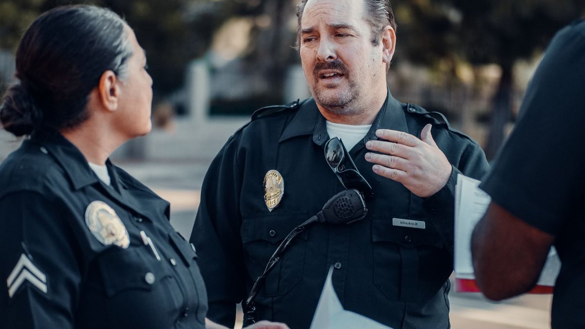 Government Considers Three Officers for Police Chief Role Three police officers engage in conversation outdoors, showcasing teamwork.