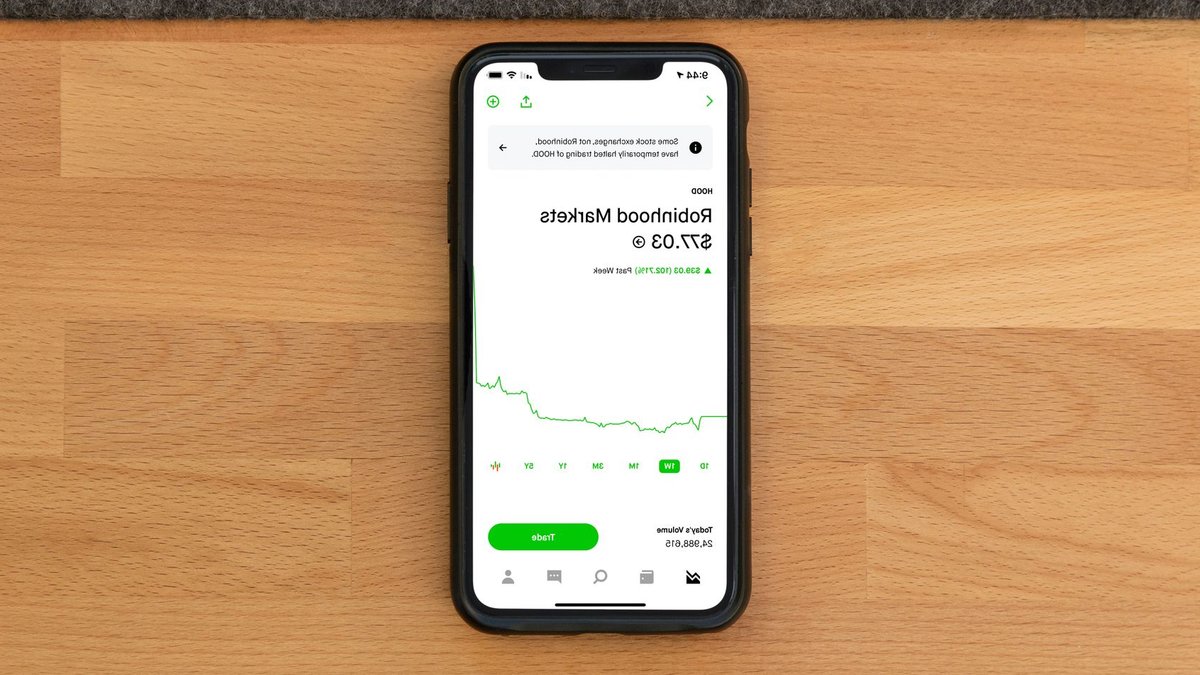 Stock trading app on smartphone displaying Robinhood Markets price on wooden desk.
