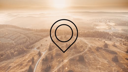 Eine Drohnenaufnahme einer weitläufigen Landschaft aus Wiesen, Wäldern und Bergen mit der Zeichnung eines Markierungszeichens im Vordergrund. Dieses Bild dient als Symbolbild für Sehenswürdigkeiten.