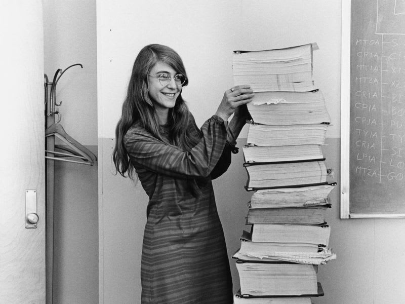 Margaret Hamilton stands next to a stack of program listings from the Apollo Guidance Computer in a photograph taken in 1969 (Wikimedia Commons)