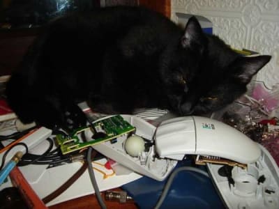 Black cat sleeps atop a pile of electronics, including a computer mouse.
