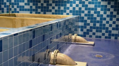 Bild på en blåkakelfärgad vattenbassäng, med rör som utgår från väggen och dyker i golvet.