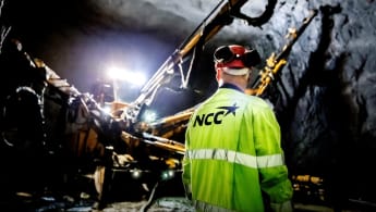 En yrkesarbetare och borrmaskiner uppehåller sig i en upplyst tunnel.