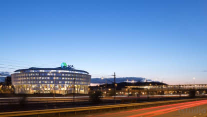 Kvällsmörk himmel. I bakgrunden SCA-huset. I förgrunden väg och järnväg i rörelse.